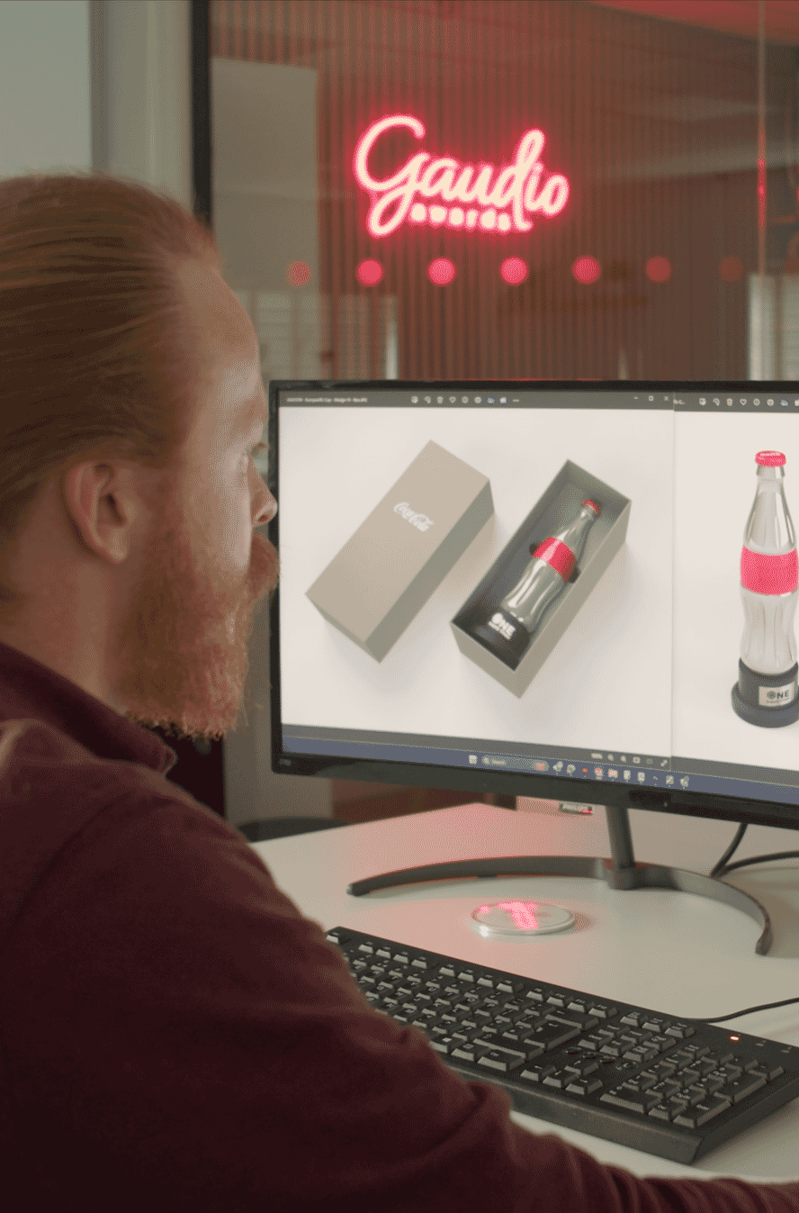 A designer sits at a computer working on a 3D trophy design for Coca Cola