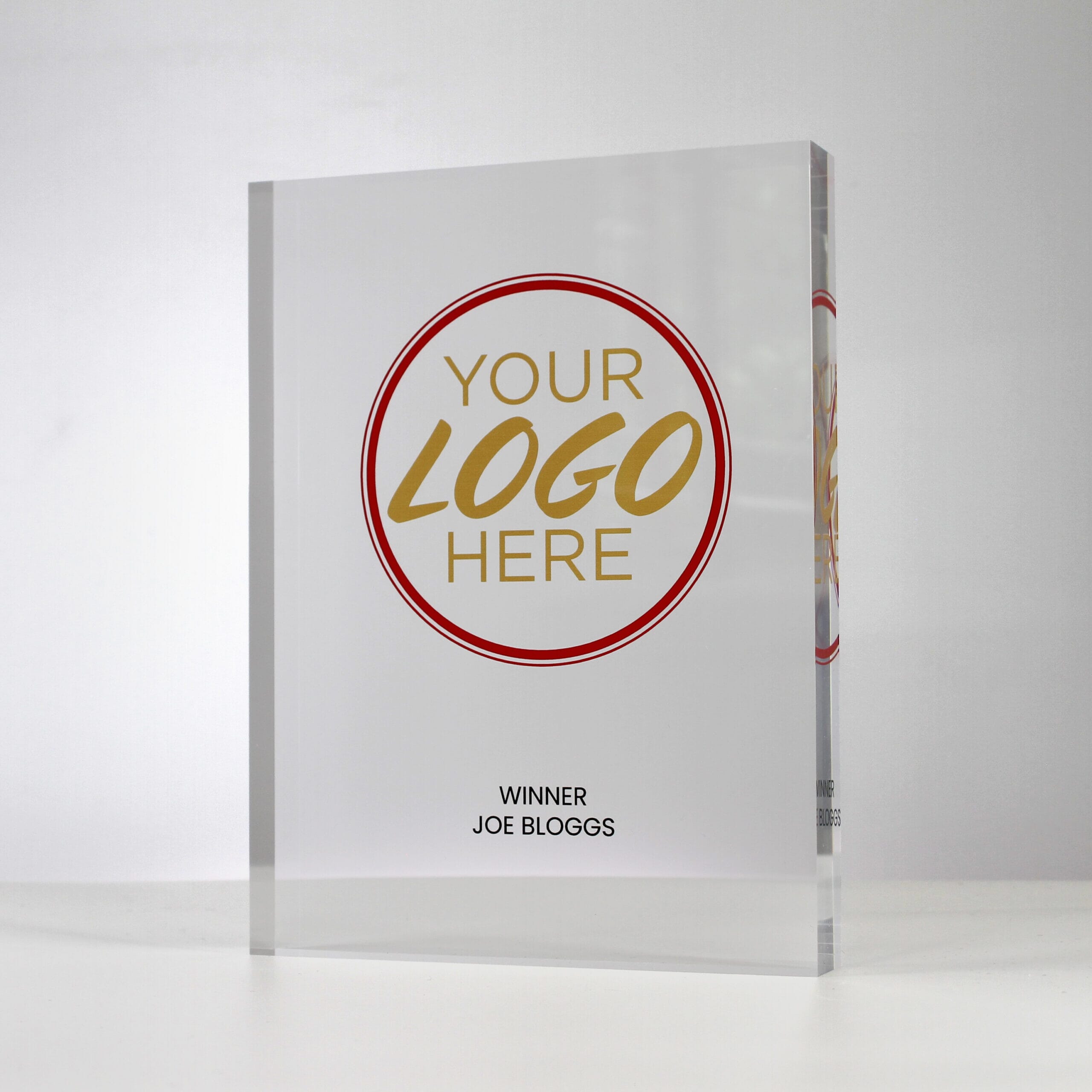A large custom acrylic trophy with 'Your Logo Here' printed in gold and red, and 'Winner Joe Bloggs' printed in black