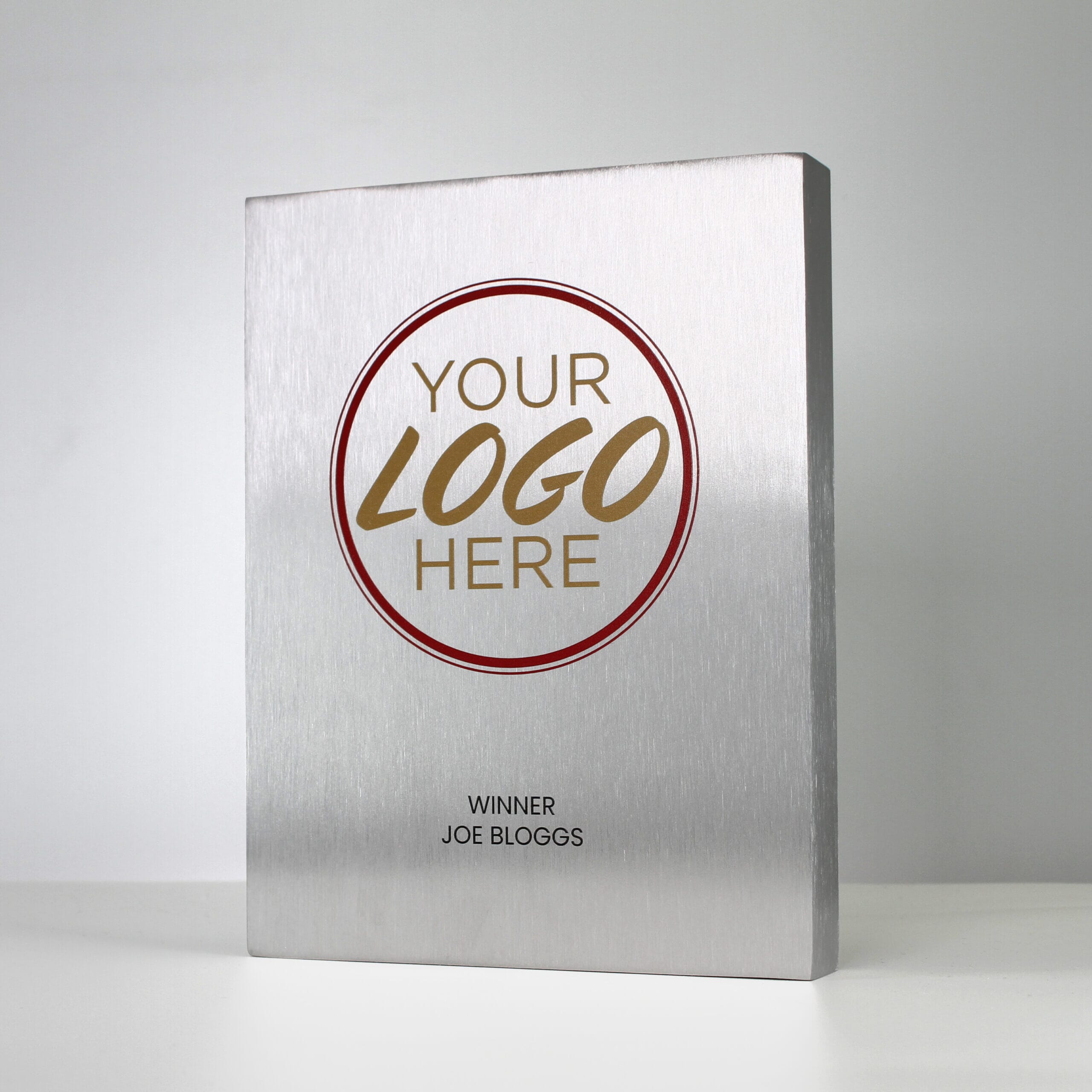 A large custom metal trophy with 'Your Logo Here' printed in gold and red, and 'Winner Joe Bloggs' printed in black