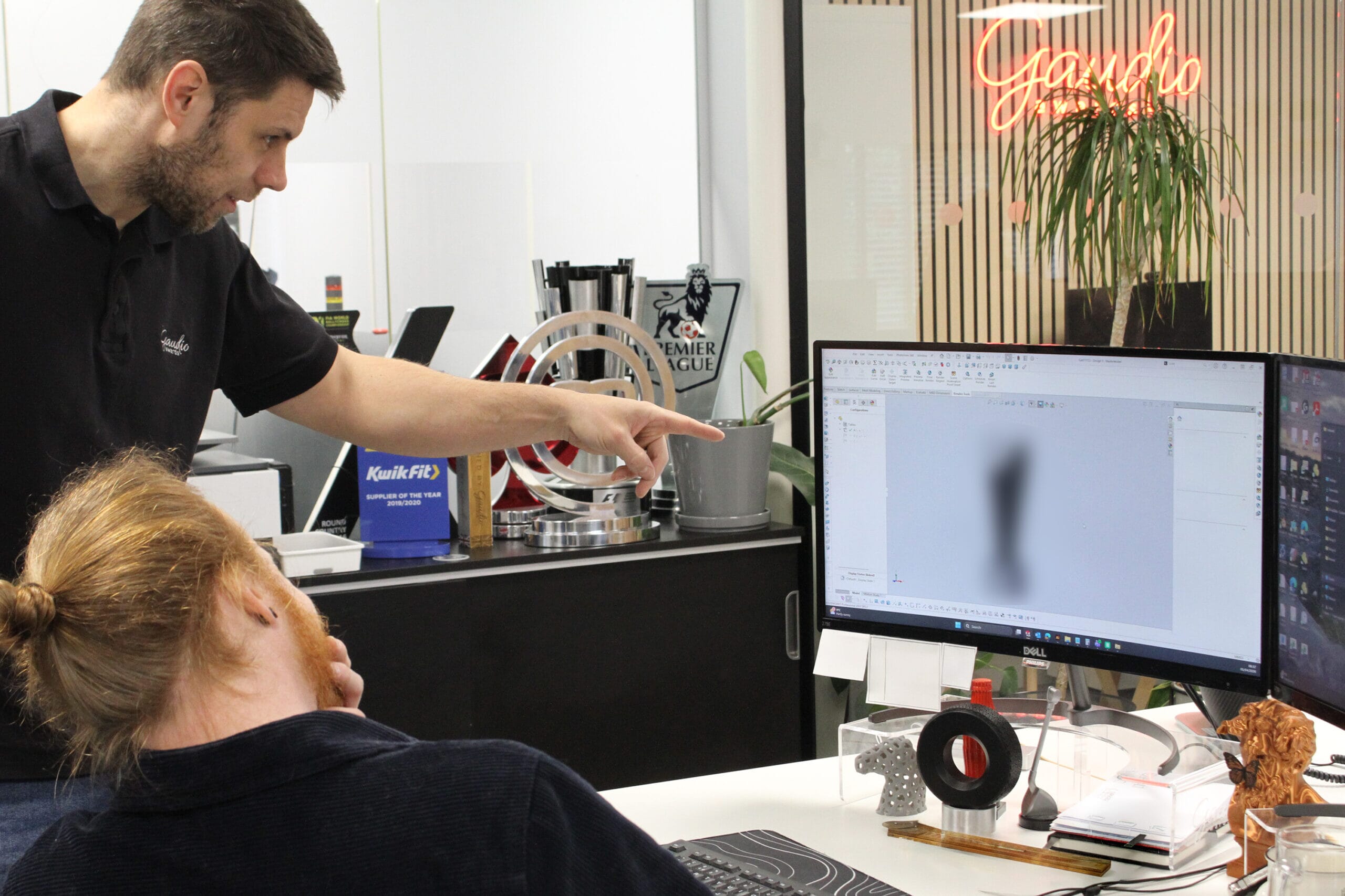 a custom trophy maker points at a design on a computer screen
